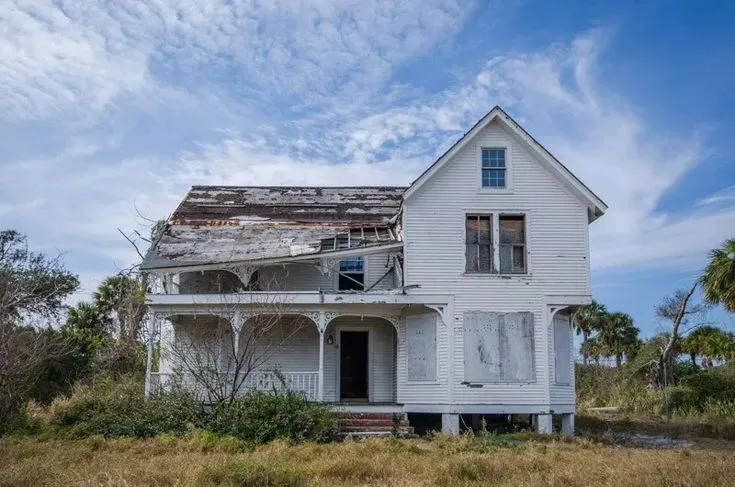 Distressed old white house with a damaged roof and boarded windows